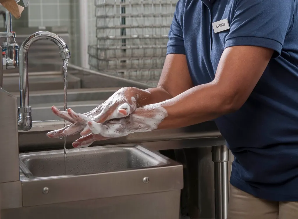 A food service worker washing hands at a sink