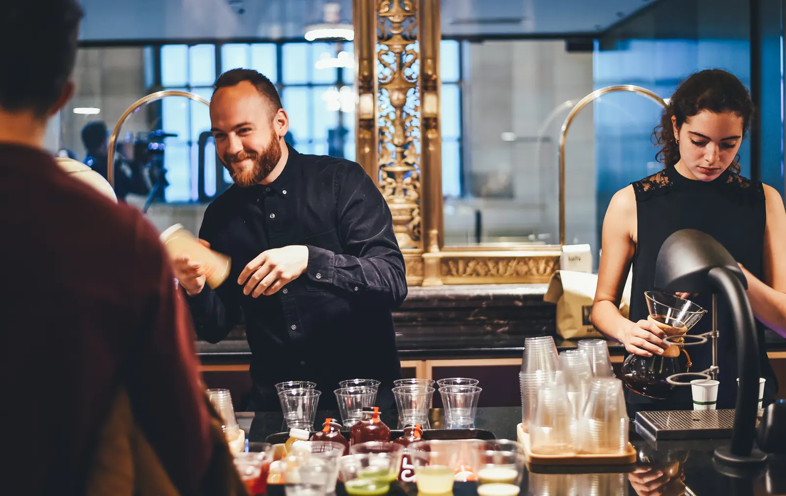 Two bartenders smiling while preparing drinks for customers